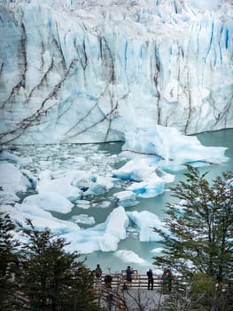 Spectators admire a glacier and icebergs from a wooden lookout.