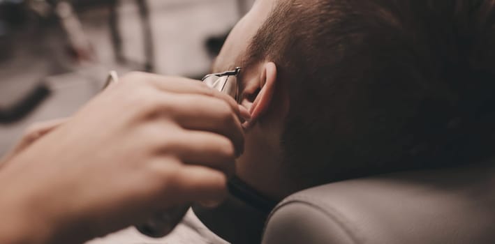 Getting perfect shape. Close-up side view of young man getting beard haircut by hairdresser