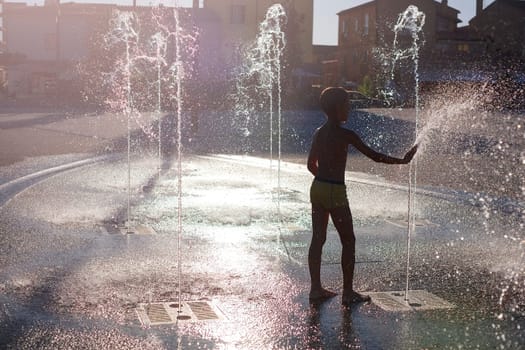 Children in the city in summer in abnormally hot weather splash and have fun in the stone fountain. Boy play in spray of water.