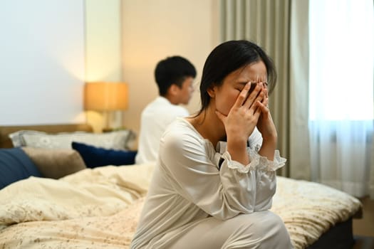 Young woman sitting and crying on bed after argument with her husband. Relationship problems concept.