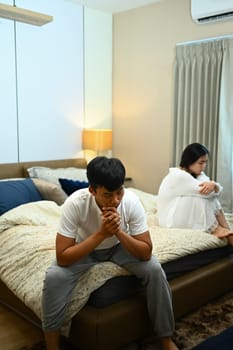 Sad thoughtful man sitting on bed after arguing with girlfriend. Conflict and relationship concept.