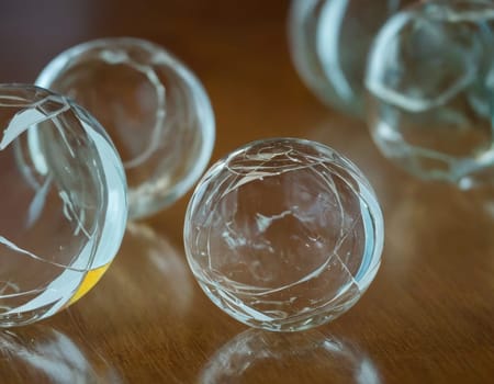 A group of glass balls are sitting on a wooden table. The balls are all different sizes and are arranged in a circle. AI generation