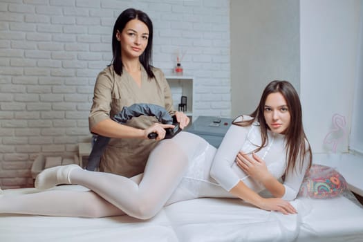 Woman in special white suit getting anti cellulite massage in a spa salon. LPG, and body contouring treatment in clinic.Reset body weight with LPG massage.