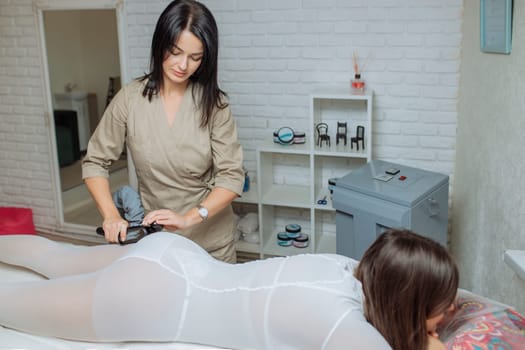 Woman in special white suit getting anti cellulite massage in a spa salon. LPG, and body contouring treatment in clinic.Reset body weight with LPG massage.