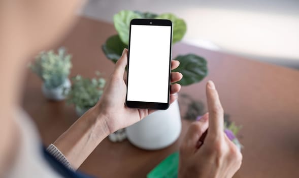 Simulated image of a blank white screen mobile phone Woman using mobile phone on table at home.