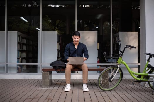 A young Asian businessman rides a bicycle to work. Use a reusable water bottle. Working outside of the office using a laptop The concept of saving energy and reducing pollution to the environment..