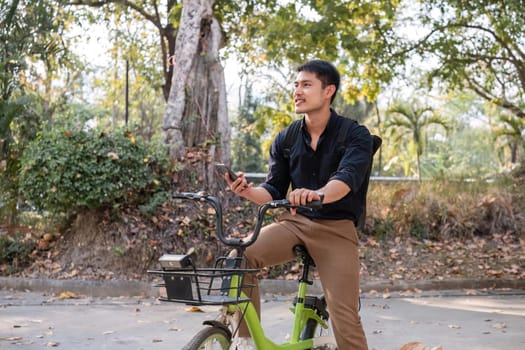 A young Asian businessman rides a bicycle to work. Standing outside the office talking on the phone and talking about business. Concept of reducing energy and reducing air pollution..