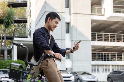 A young Asian businessman rides a bicycle to work. Standing outside the office talking on the phone and talking about business. Concept of reducing energy and reducing air pollution..