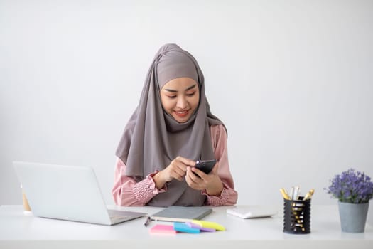Smiling Muslim business woman Wearing a hijab while chatting online on a work desk in the office..