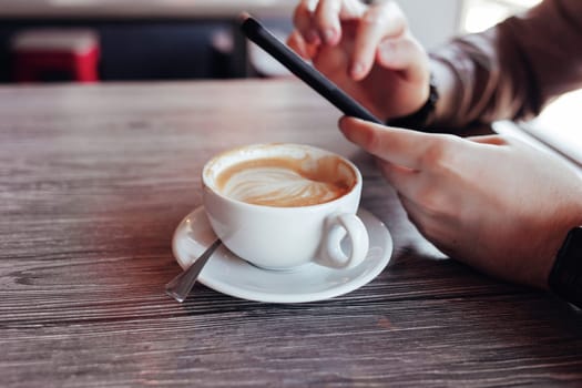 Close-up of a man's hands holding a cell phone in a cafe. a hipster man watches a video on his mobile phone during a coffee break