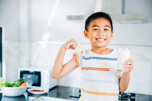 Cheerful Asian little boy holds milk in kitchen, smiling brightly. Portrait of cute son enjoying drink. Joyful child sips calcium-rich liquid, radiating happiness at home give me.