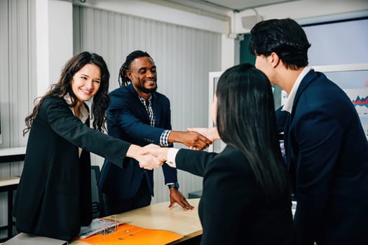 In an office, business people shake hands to celebrate an agreement. Colleagues, including marketing experts, successfully conclude a deal after a productive meeting. Teamwork