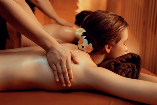 Caucasian couple customer enjoying relaxing anti-stress spa massage and pampering with beauty skin recreation leisure in warm candle lighting ambient salon spa at luxury resort or hotel. Quiescent