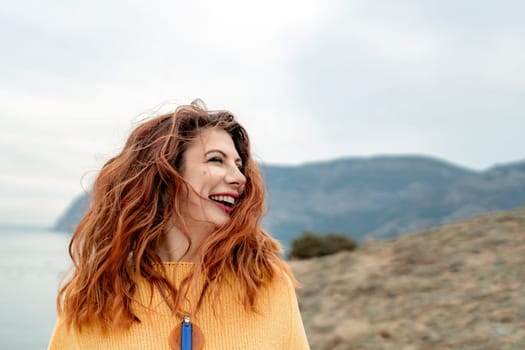 Portrait windswept hair happy woman against a backdrop of mountains and sea. Daylight illuminates the tranquil outdoor setting.