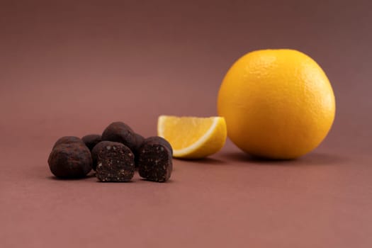 Vegan Raw Sweet Balls made of Organic Cocoa beans with Dry Citrus Fruits on Brown Background. Orange is beside. Horizontal Plane. Healthy Food, Dessert. High quality photo