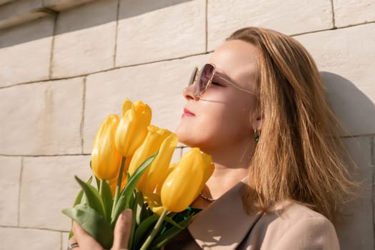 Woman holding yellow tulips, leaning against stone wall. Women's holiday concept, giving flowers