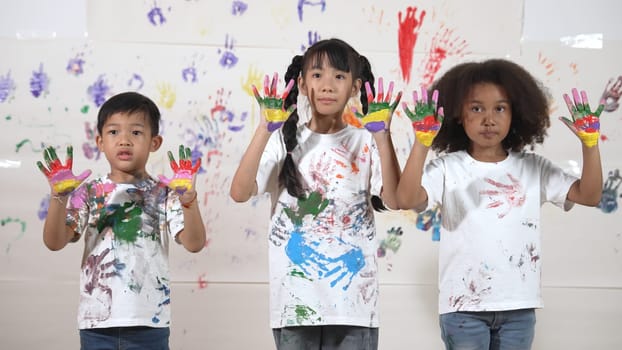 Diverse students put hands up together show colorful stained hands. Group of multicultural learner standing at white background with stained hands while looking at camera in lively mood. Erudition.