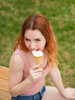 Young beautiful red-haired woman smiling with braces and eating an ice cream cone outdoors. Vertical photo