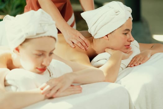 A couple of beautiful young woman with white towel lie on comfortable spa bed during receive relaxing body massage by professional masseur surrounded at spa salon. Gray background. Tranquility.