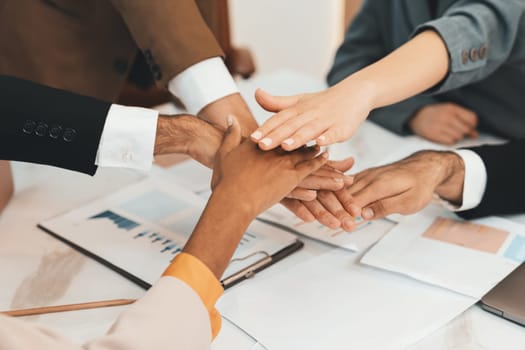 Top view of corporate diverse businesspeople putting hands together on meeting table with document scatter around at business meeting room. Represented unity, cooperation, collaboration. Ornamented.