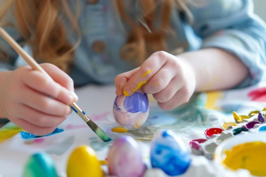A young girl is painting a yellow and blue egg. She is using a brush to apply the paint