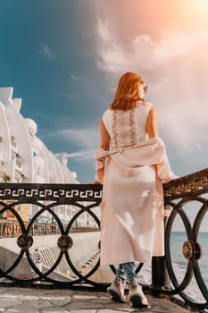 Woman travel sea. Young Happy woman in a long red dress posing on a beach near the sea on background of volcanic rocks, like in Iceland, sharing travel adventure journey