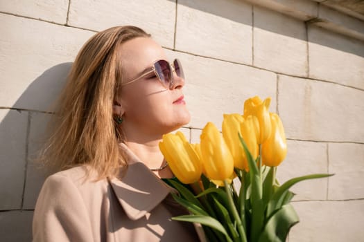 Woman holding yellow tulips, leaning against stone wall. Women's holiday concept, giving flowers