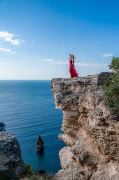 A woman in a red flying dress fluttering in the wind, against the backdrop of the sea