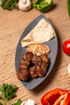 Grilled meat and vegetables on a rustic wooden table with soft flatbread. Succulent meat, tender veggies, vibrant tomatoes, peppers, mushrooms, onions create a delicious meal.