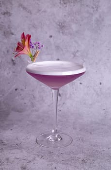 Elegant image of a pink cocktail in a glass with a flower garnish on a gray background, exuding class and sophistication.