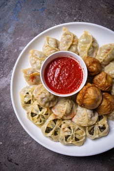 A delicious assortment of Uzbek dumplings with meat, pumpkin, and greens served on a plate with a side of red sauce