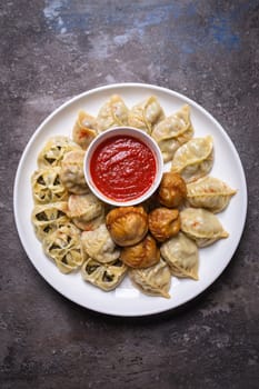 A delicious assortment of Uzbek dumplings with meat, pumpkin, and greens served on a plate with a side of red sauce