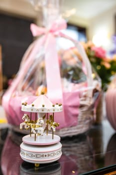 Elegant baby shower gift basket filled with essentials and toys, adorned with a pink bow and cute carousel. Perfect for invitations, announcements, or as a thoughtful gift guide item.