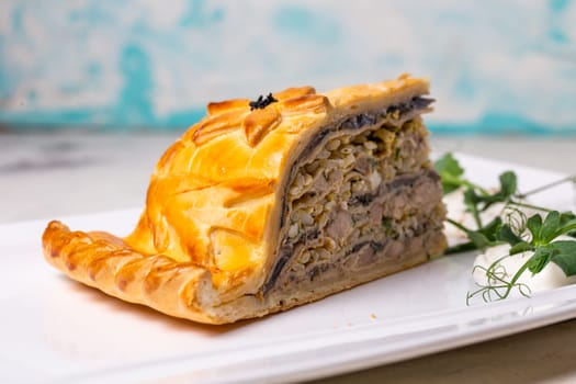 A delicious slice of savory meat pie with golden crust, layers of meat, veggies on a plate with sour cream and herbs.