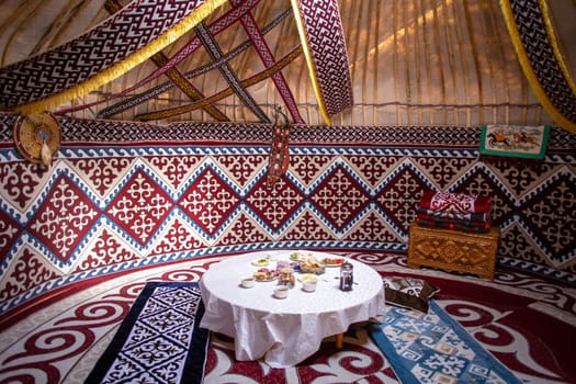 Interior of a kazak yurt with felt carpets, furniture, and a table. Traditional nomadic dwelling with white tablecloth.