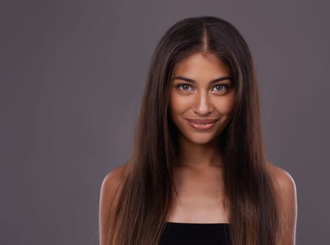 Portrait, hair care and Indian woman with cosmetics, treatment and grooming routine on a grey studio background. Face, person and model with volume or texture with keratin and healthy shine with glow.