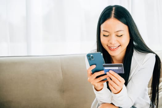 Woman on sofa uses smartphone and credit card for online shopping. Engaged in ordering banking and purchasing goods or services. Modern technology for convenient shopping.
