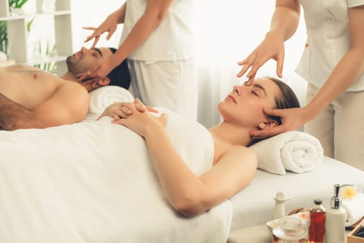 Caucasian couple enjoying relaxing anti-stress head massage and pampering facial beauty skin recreation leisure in dayspa modern light ambient at luxury resort or hotel spa salon. Quiescent