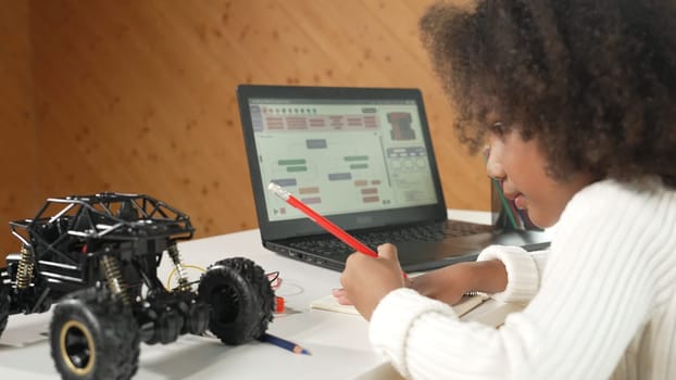 African girl writing car model structure while laptop display code. Smart student working by using laptop develop program or learning programing engineering prompt Erudition in STEM class work.