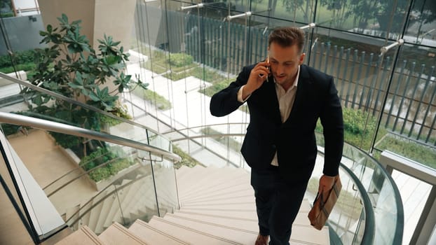 Smart businessman walking up spiral stair case and calling manager by using smart phone. Top view of manager talking marketing team by using telephone while going up stair at modern building. Urbane.