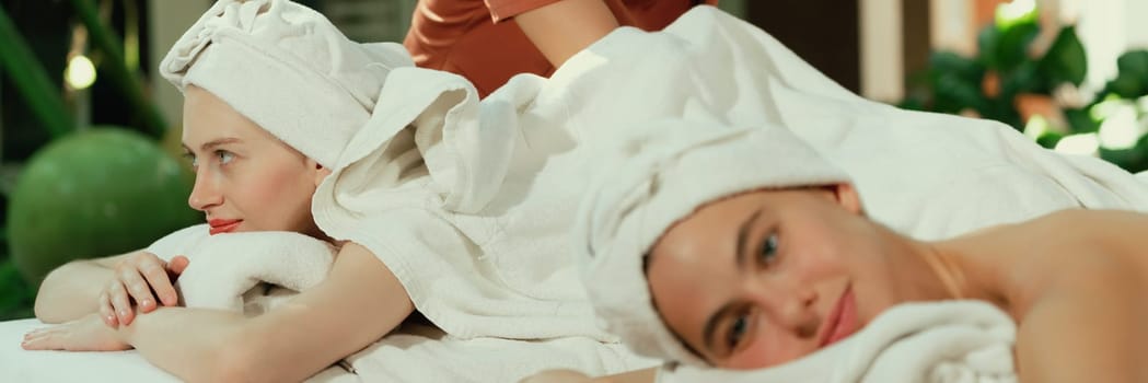 A portrait of a couple of a beautiful young caucasian woman with white towel rest on comfortable spa bed with relaxation while having body massage with professional masseur at spa salon.Tranquility.