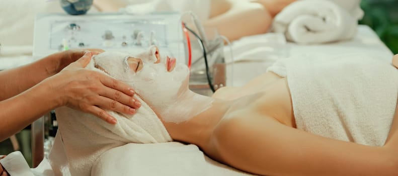 Beautiful young women lie on spa bed while having facial massage from professional doctor. Attractive female with beautiful skin surrounded by electric facial machine. Tranquility.