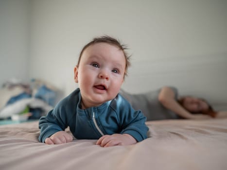 A three-month-old boy lies on his stomach on the bed and his mother sleeps behind him. Postpartum depression
