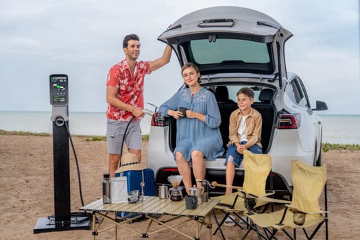 Family vacation trip traveling by the beach with electric car, happy family recharge EV car, enjoying outdoor camping coffee. Seascape travel and eco-friendly car for clean environment. Perpetual