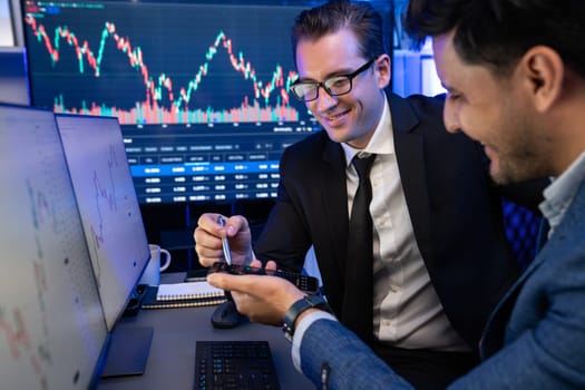 Two stock exchange traders comparing dynamic investment graph via phone and pc with high profit in currency rate. Showing financial benefit data on monitor screen in neon light at workplace. Sellable.