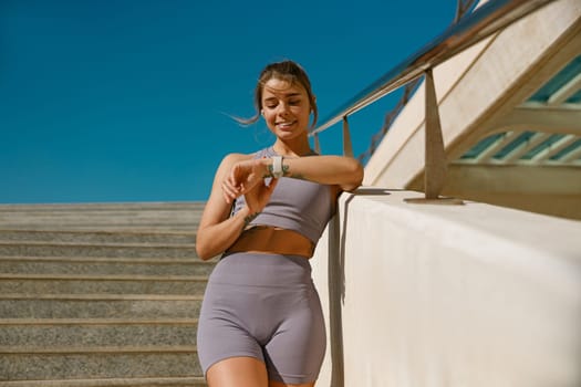 Young woman in sportswear looking on smartwatch before exercising. Outdoor sports in the morning