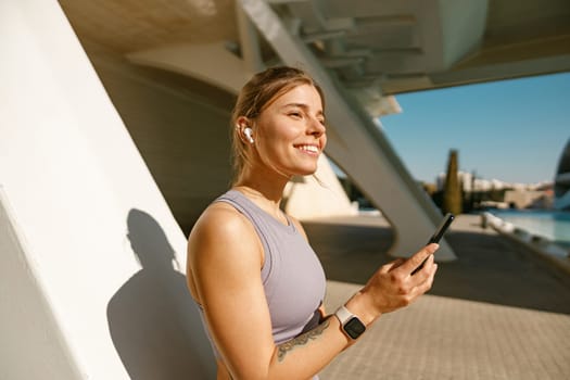 Fit woman in sportswear standing outdoors after training and use mobile phone