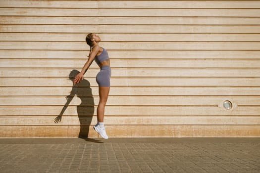 Young fit woman in sportswear leaping in the air with wall backdrop outdoors. High quality photo