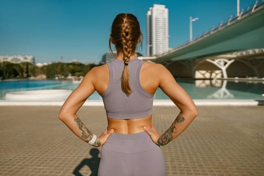 Back view of female athlete in sportswear have a rest after morning jogging outside