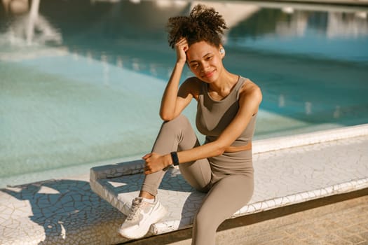 Smiling female athlete in sportswear have a rest after morning jogging outside and looks camera